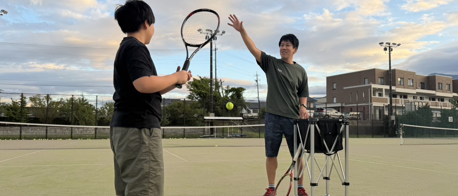 夕暮れのテニスコートでレッスンをするコーチと参加者