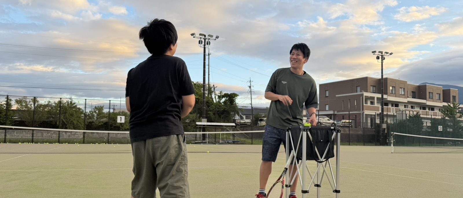 夕暮れのテニスコートでレッスンをするコーチと参加者