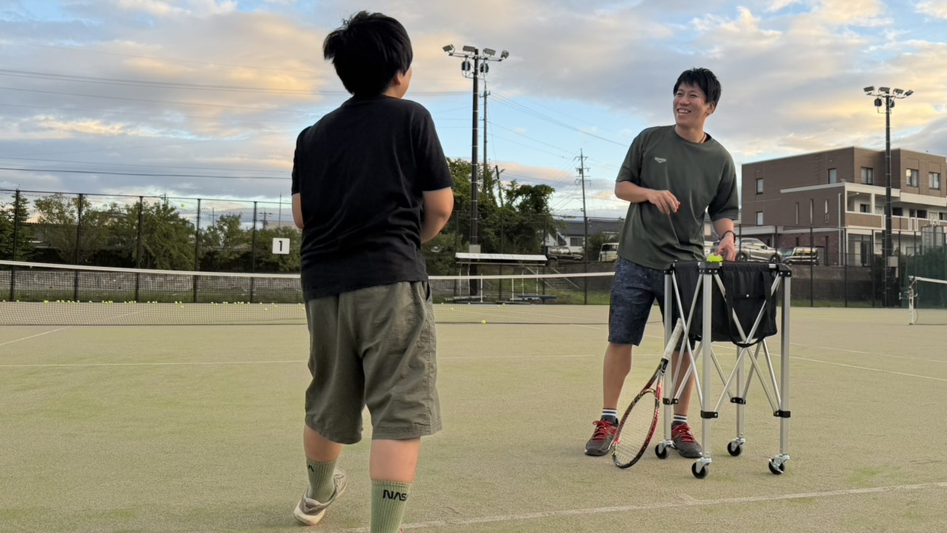 夕暮れのテニスコートで笑顔でレッスンをするLIFE TENNISのコーチと参加者